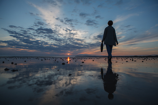 Sillhouette of a woman walking towards the sun on the ocean coastline reflected in a wet send, Normandy