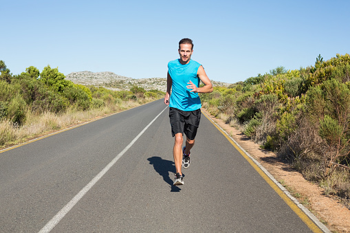 Fit man jogging on the open road on a sunny day