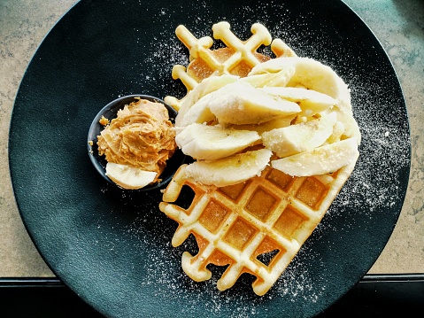 Amazing tasty dessert belgian waffles with banana and peanut butter in restaurant