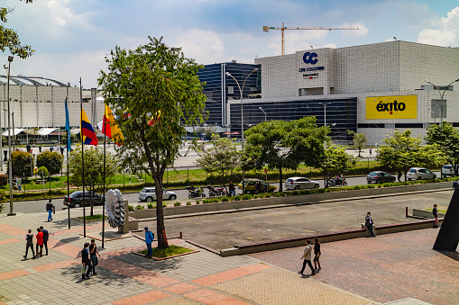 Bogotá, Colombia - February 16, 2017: Looking from a pedestrian walkway on Avenida El Dorado or Calle 26, towards the Gran Estación shopping mall in the Andean capital city in South America. Across the road, is the Plazoletta attached to the Mall. It is lunchtime and people can be seen either walking towards, or away from the Mall. Some cars are parked illegally on the street: it is not a place where they should be parking. The railroad track that cuts across Avenida El Dorado can also be seen. Photo shot in the early afternoon sunlight; horizontal format.