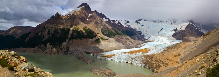 Glacier running into a dirty lake surrounded by rocky landscape
