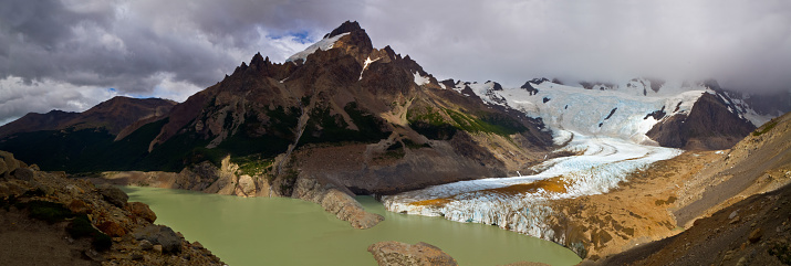 Glacier running into a dirty lake surrounded by rocky landscape