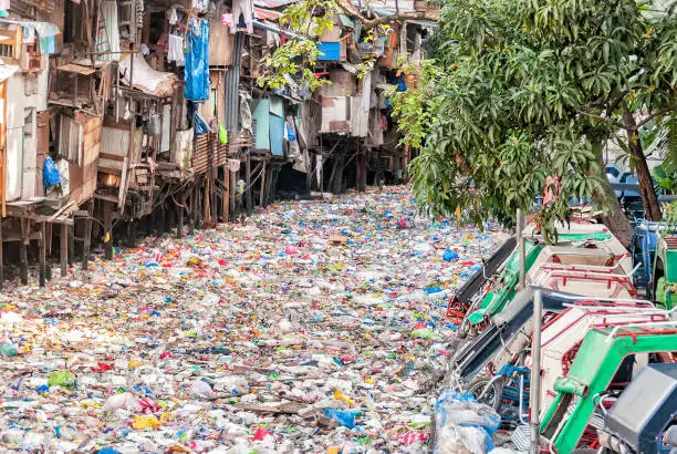 Shanties on stilts standing on garbage-filled river