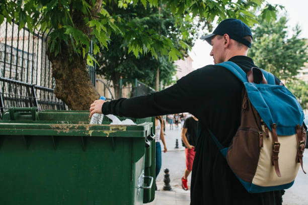 istock A tourist with a backpack and in a baseball cap on the street throws a plastic bottle into a container with waste. Care for the environment. Eco friendly. Tourist. 816726514