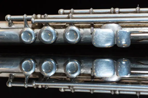 Photo of symphonic music concept - beautiful closeup on western concert flute lies on the pure black mirror surface, middle section of instrument with majority of keys, marching, orchestra concerts, macro