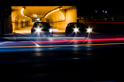 Night traffic on city streets. Cars queued at tunnel exit waiting at intersection while driving vehicles moving past leaving color light trails