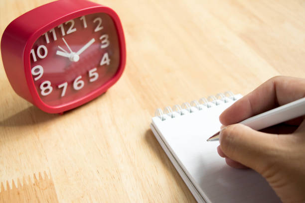 istock Man hold the pen with book and red clock on wooden table background 816833070