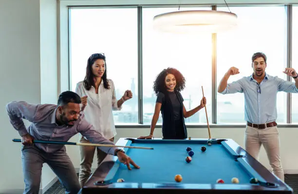 Young men and woman playing billiards at office after work. Business colleagues involving in recreational activity after work.