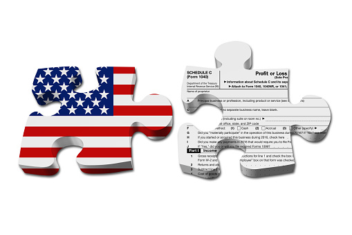 Understanding how to do your business taxes, Two puzzle pieces with the flag of the USA and a US Federal tax Schedule C for 1040 income tax form isolated over white