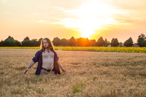 Young caucasian - nordic man with blond and long hairs among grain field at sunset