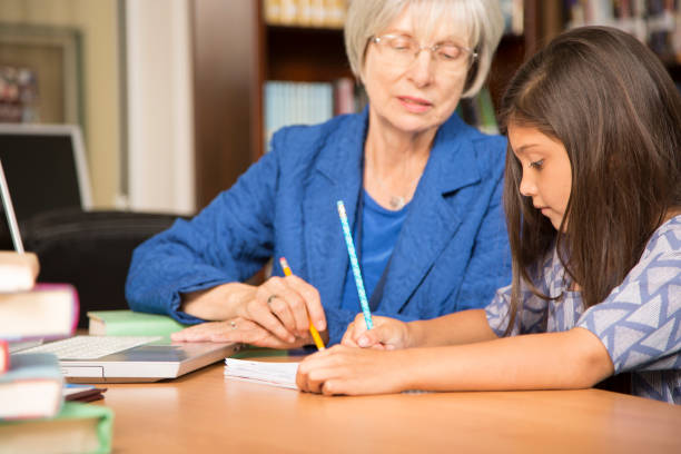 istock Teacher, mentor helps elementary-age schoolgirl with homework. 816892560