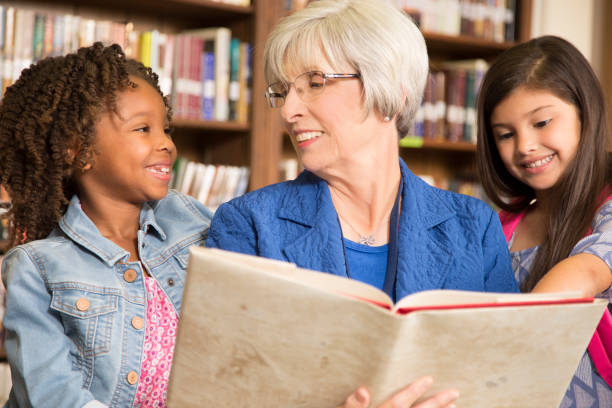 istock Teacher, librarian reads book to elementary students in library or classroom. 816892588