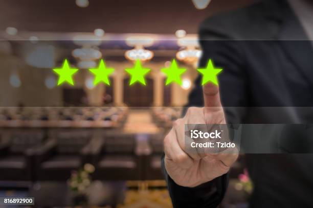 Businessman Pointing Five Star Symbol To Increase Rating Of Hotel Over Abstract Blurred Photo Of Conference Hall Or Seminar Room With Attendee Background Business Evaluation Concept Increase Rating Stock Photo - Download Image Now