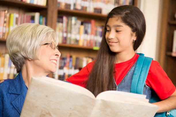 istock Teacher, librarian reads book to elementary student in library or classroom. 816893142