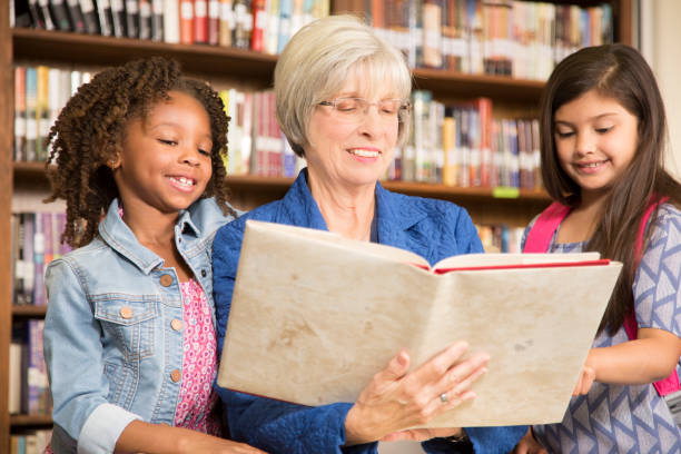 istock Teacher, librarian reads book to elementary students in library or classroom. 816897608