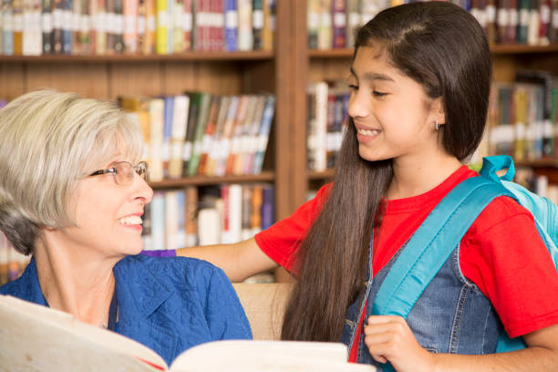 istock Teacher, librarian reads book to elementary student in library or classroom. 816897928