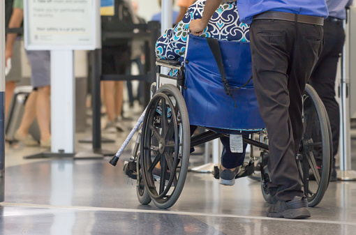 Passengers on wheelchair pushed by an assistant in an airport