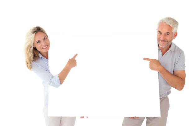 Happy couple holding and pointing to large poster on white background