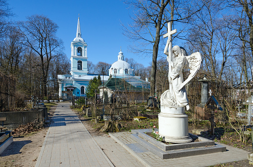 Saint Petersburg, Russia - May 2, 2017: Smolensk Cemetery in St. Petersburg, Russia. Tombstone sculpture (angel with cross) on grave. Church of Smolensk Icon of Mother of God