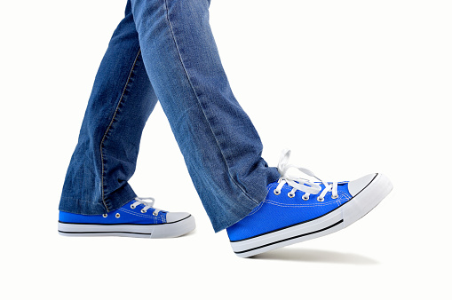 close up of steps of a person walking with sneakers and jeans isolated on white background