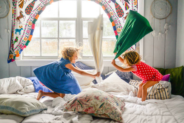 Pillow Fight Two little girls, kids in a candid shot having a pillow fight in bed child behaving badly stock pictures, royalty-free photos & images