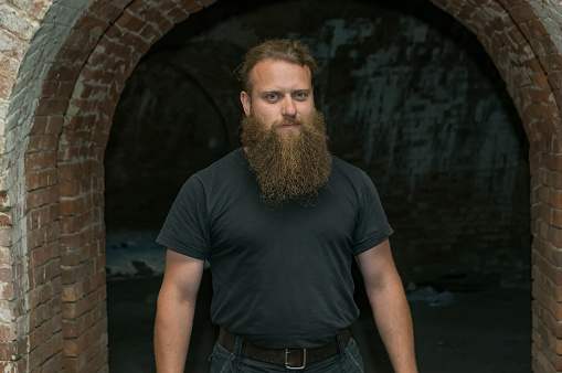 A man with a beard, against a brick arch.