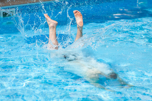 active rest, lifestyle and summer sport concept - man dives into blue pool water, splashing drops after jump and feet of swimmer on surface, entertainment in hotel or rear yard of household. descanso activo, estilo de vida y verano deporte concepto - hombre hombre inmersiones en el agua de la piscina azul, salpicando gotas después de salto y los pies del nadador en la superficie, entretenimiento en el hotel o patio trasero de casa