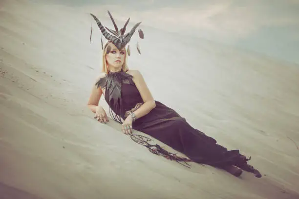 Woman with horns on her head lying on the sand in the desert.
