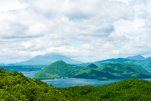 Toya Caldera, lake in beautiful volcanic landscape of Usu Volcano UNESCO Global Geopark, In the clouds in background the highest volcano Mt. Yotei Hokkaido, Japan.