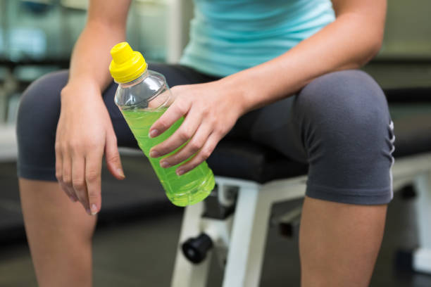 Fit woman sitting on bench holding energy drink Fit woman sitting on bench holding energy drink at the gym energy drink stock pictures, royalty-free photos & images