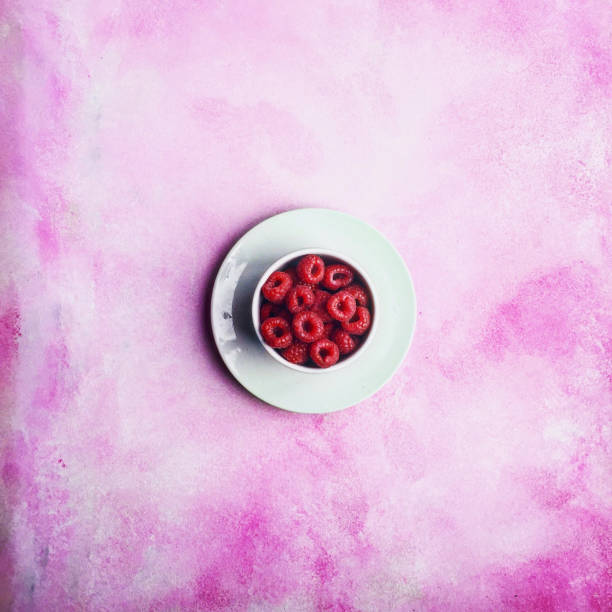 Raspberries on white plate and pink background.