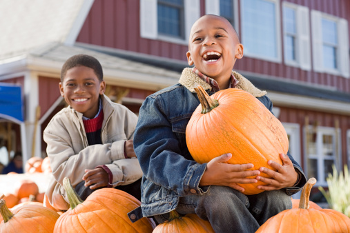 Photo of a two young children, proudly holding pumpkins that were just picked from their greenhouse.