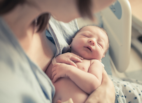 New born baby boy resting in mothers arms.