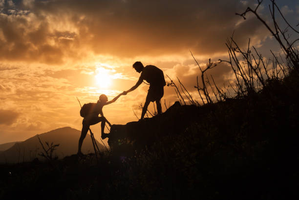 istock People helping each other hike up a mountain at sunrise. 817147756