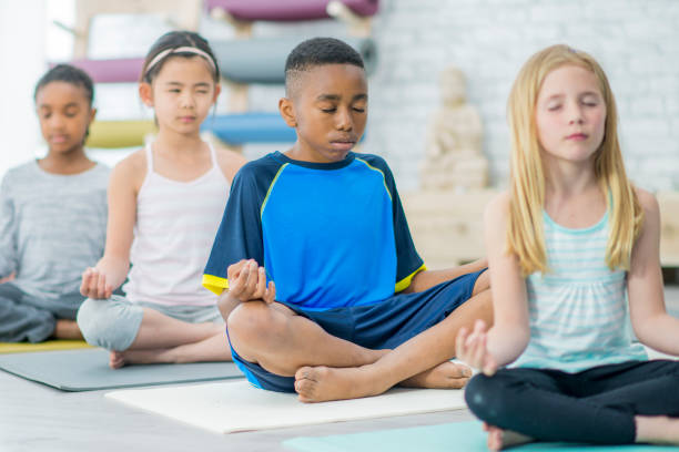 Elementary School Meditation A multi-ethnic group of children are indoors in a health club. They are wearing casual athletic clothing. They are sitting cross-legged and doing a meditation pose with their eyes closed. mindfulness kids stock pictures, royalty-free photos & images