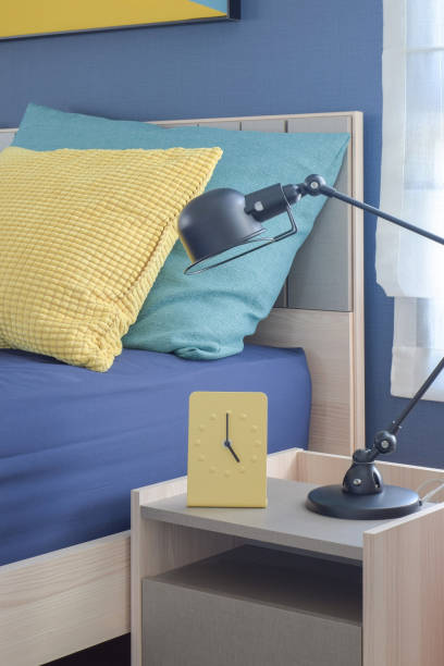 istock Yellow modern clock on bedside table with colorful pillows in background 817188836