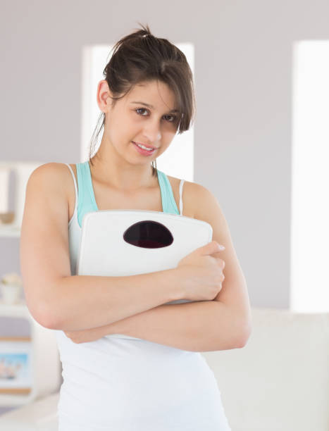 istock Fit brunette smiling at camera holding scales 817233542