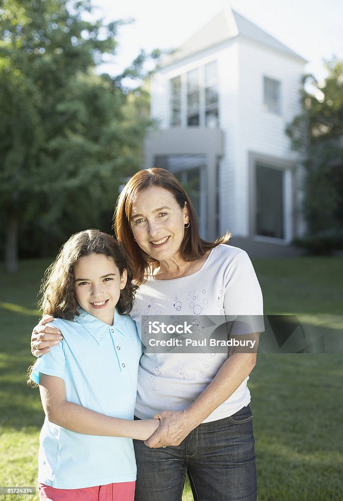 Donna e giovane ragazza in piedi all'aperto e sorridente tenendo le mani - Foto stock royalty-free di 60-64 anni