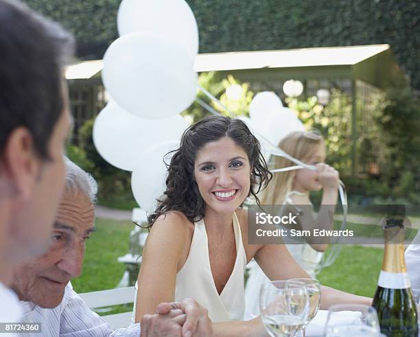 Woman Sitting At Table At Outdoor Party Smiling With People Around Her Stock Photo - Download Image Now