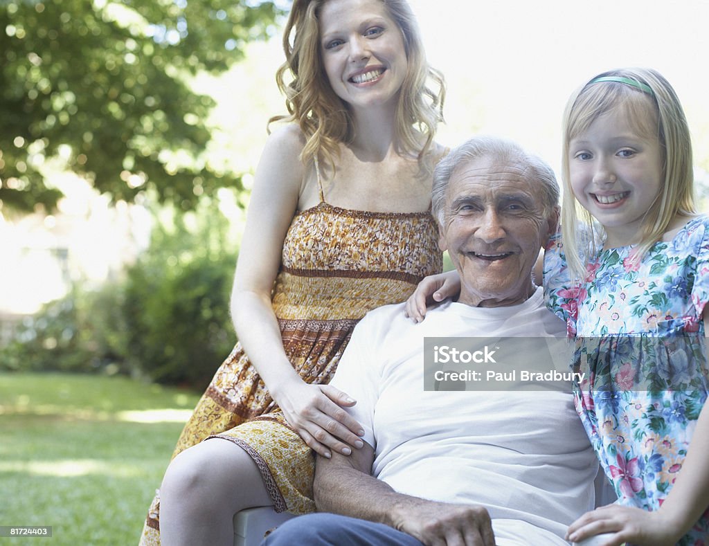 Uomo anziano con donna e giovane ragazza seduto all'aperto sorridente - Foto stock royalty-free di Figlia femmina