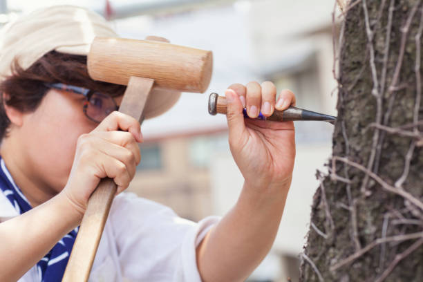 A close-up photo of a Japanese woman sculptor while carving buddha face on a tree.