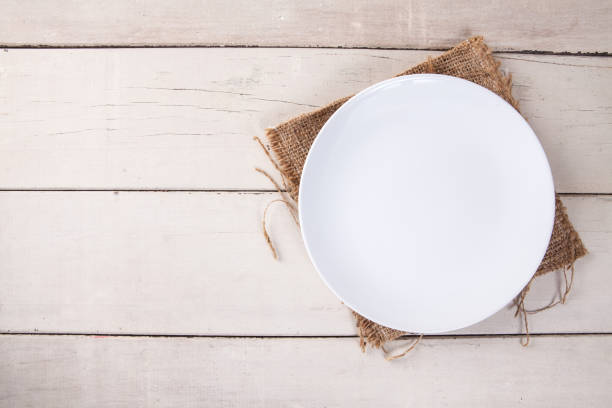 istock Top view of empty white plate put on sack and white wood table with space for copy. 817263472