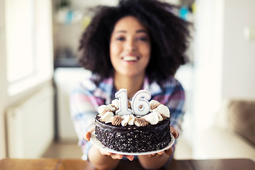 Smiling woman holding birthday cake with candles, looking at camera.