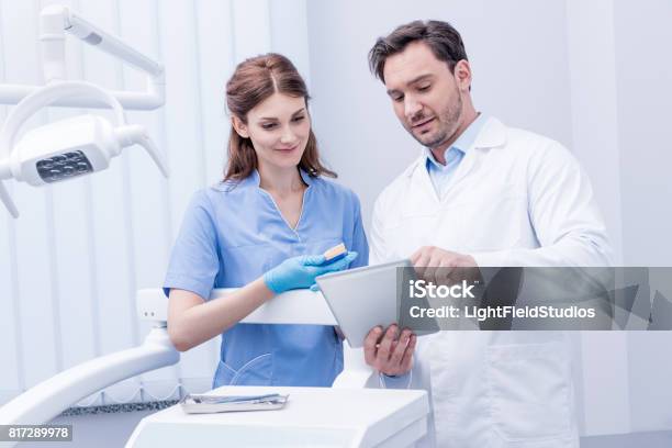 Portrait Of Young Dentists Discussing Work Together And Using Tablet In Dental Clinic Stock Photo - Download Image Now
