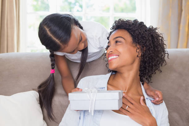 istock Pretty mother sitting on couch with daughter offering a gift 817290382