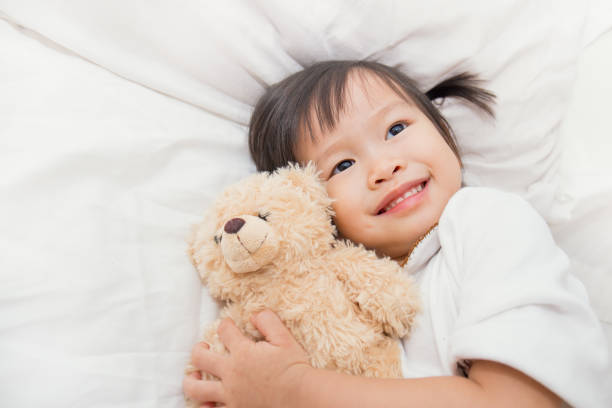 niedliche kleine kind asiatin umarmt teddybär im bett - child asian ethnicity little girls toddler stock-fotos und bilder