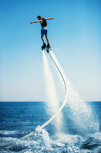 Closeup rear view of a young man enjoying flyboarding session at sea on a sunny summer day.