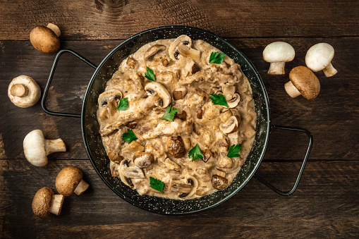 Mushroom beef stroganoff, with cremini and champignons, in a frying pan, shot from above on a dark rustic texture with a place for text