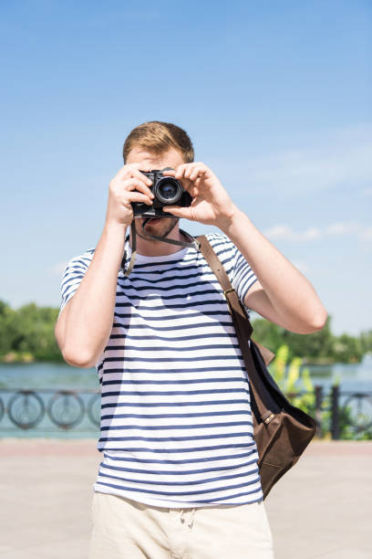 istock Young man with backpack holding camera and photographing while standing outdoors 817325368