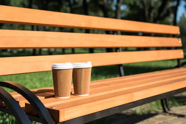 Photo of Close-up view of two disposable coffee cups on wooden bench in park